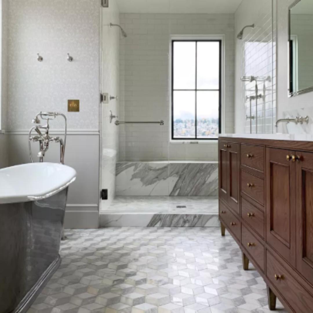 Modern bathroom featuring a freestanding metallic bathtub, marble walk-in shower, and double-sink vanity with dark wood and brass hardware—showcasing how natural textures and warm metals elevate a gray-toned space into a cozy, contemporary retreat.